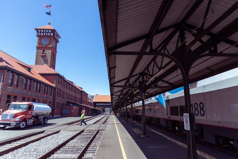 A train platform. with a train parked on the right, and the station building on the left, topped by a 'UNION STATION' clock tower