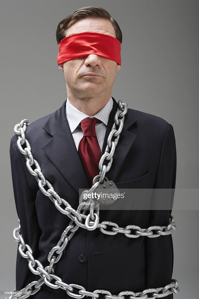 businessman-wearing-blindfold-wrapped-in-chains-picture-id200544524-002