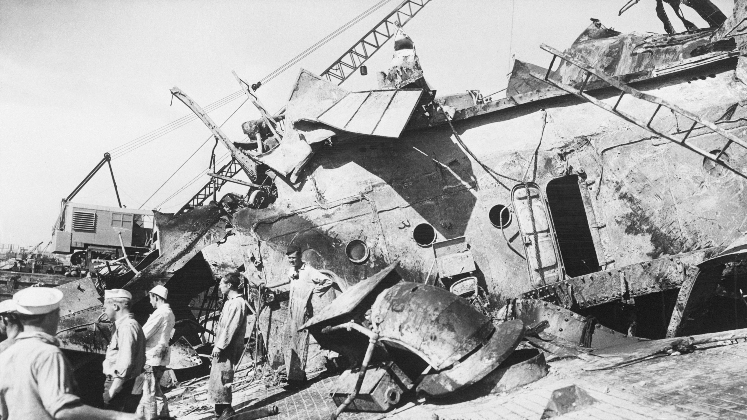 Men stand on the damaged wreck of a warship.