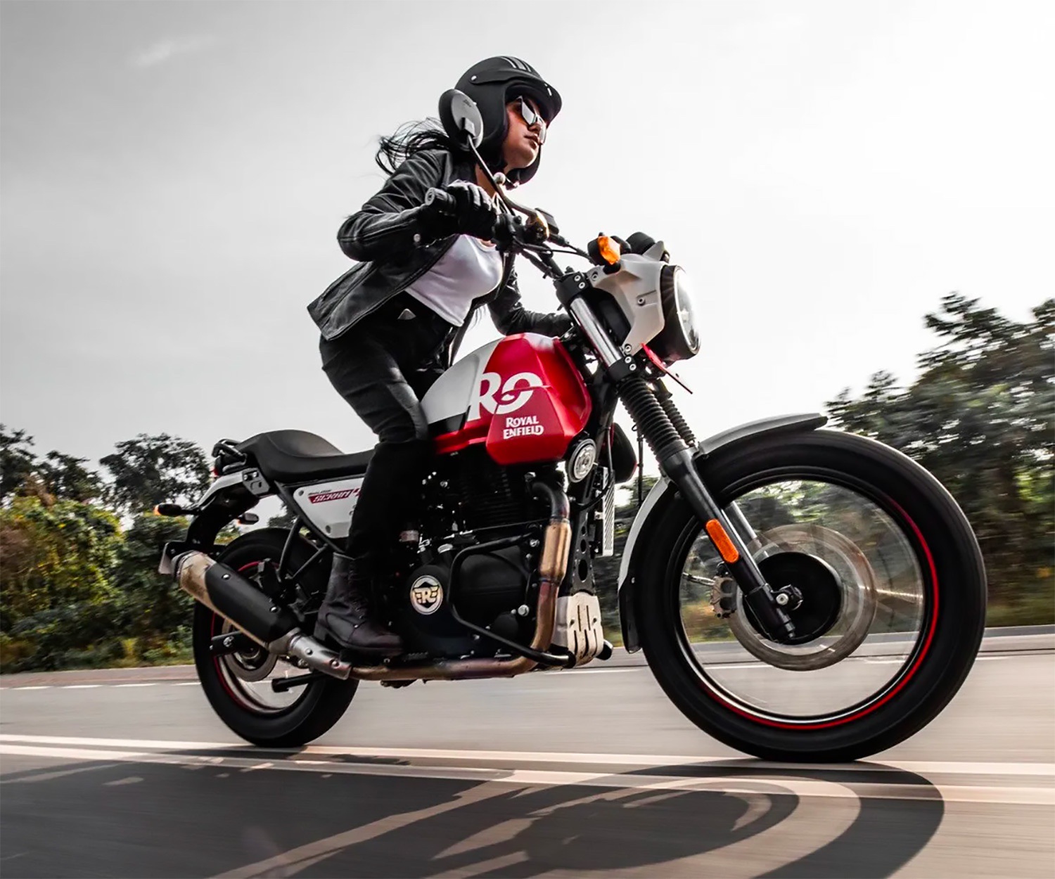 A 2022 Royal Enfield Scram 411 motorcycle rides on a road with the rider standing up on the pegs