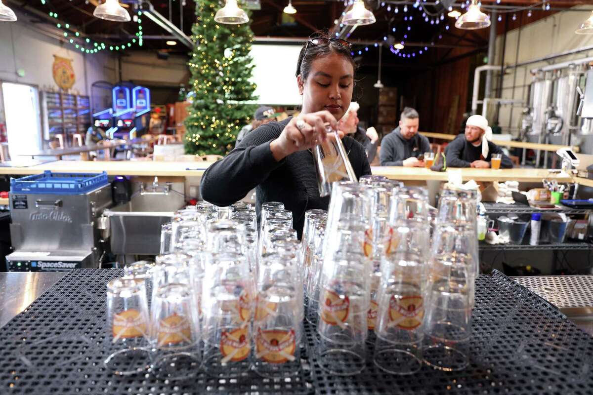 Bartender Maya Arteseros grabs a glass while working at Anchor Public Taps. The taproom is decorated with Christmas decor for its Christmas in July promotion, which was announced after the brewery discontinued its beloved Christmas Ale last month. 