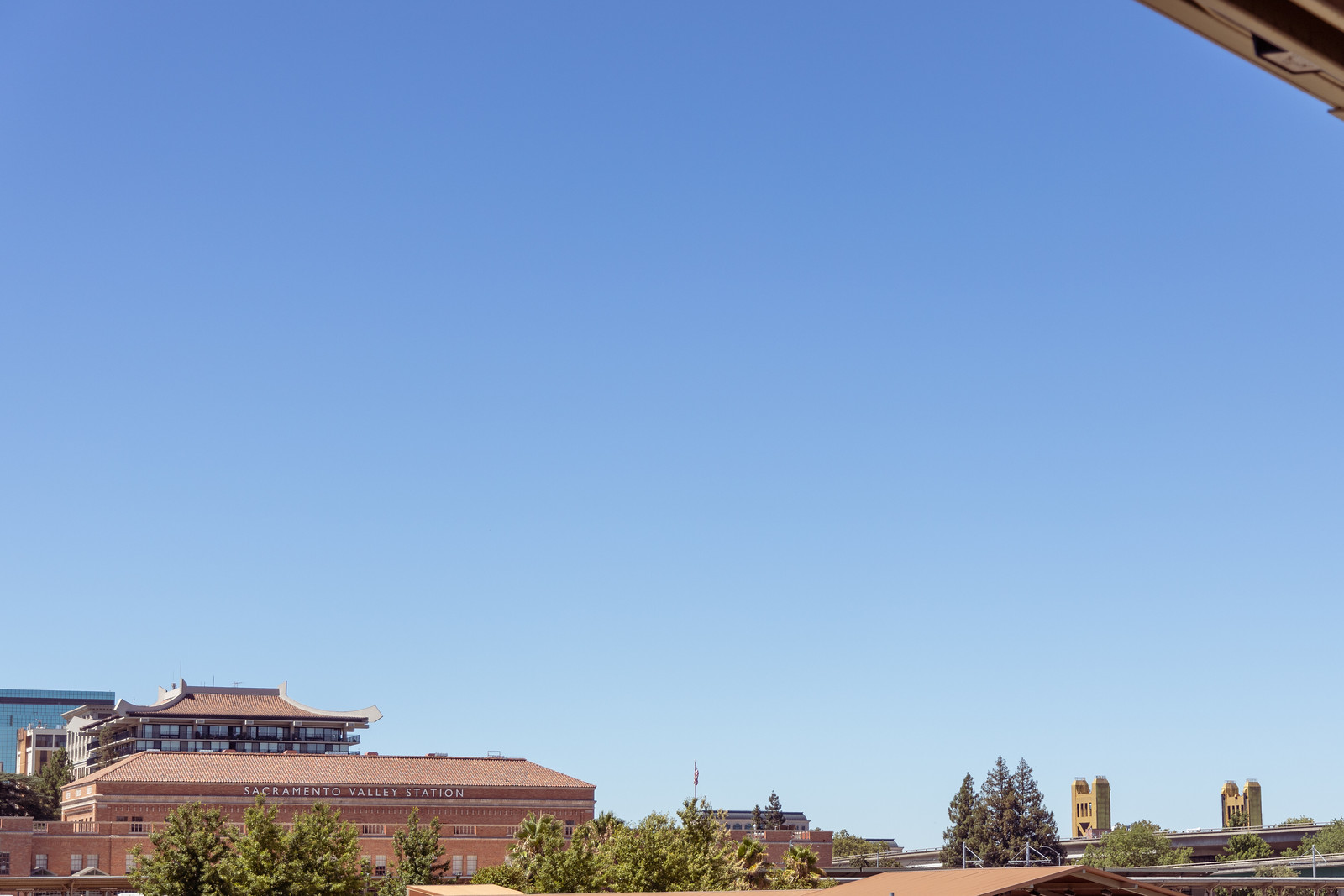 A brick building labeled 'Sacramento Valley Station' near a yellow bridge, a larger pagoda-style building, and a glass office building beyond. The frame is dominated by the blue sky