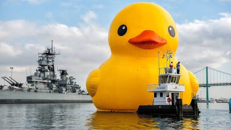 A giant rubber duck floats next to several ships.