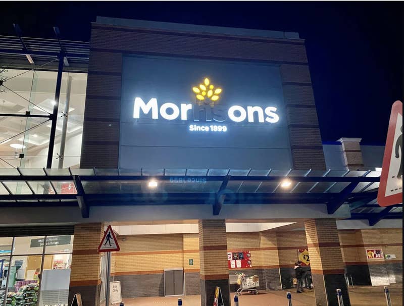 Sign of 'Morrisons' grocery store at night with illuminated branding above entrance